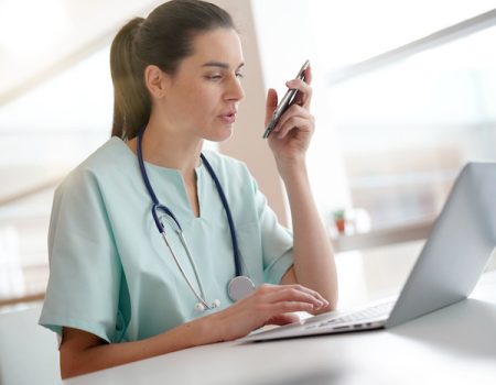 Nurse working on laptop computer and recording on dictaphone